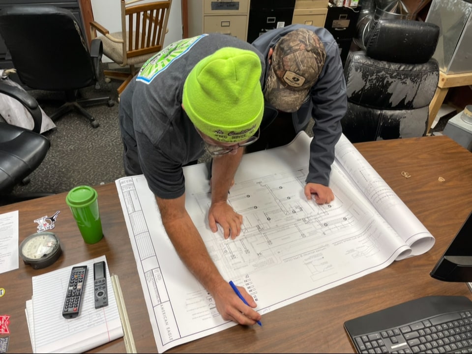 Two Air Conditioning Service team members hovering over a construction layout plan in their office.